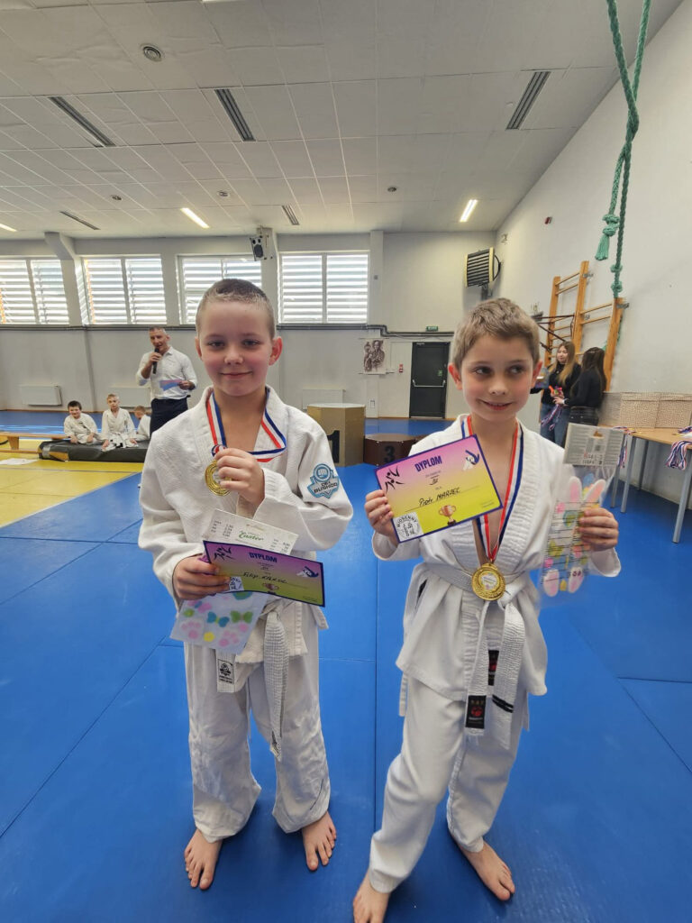 Nastolatek w judodze z powagą prezentuje medal i dyplom za zajęcie wysokiego miejsca w turnieju judo w Koszalinie.