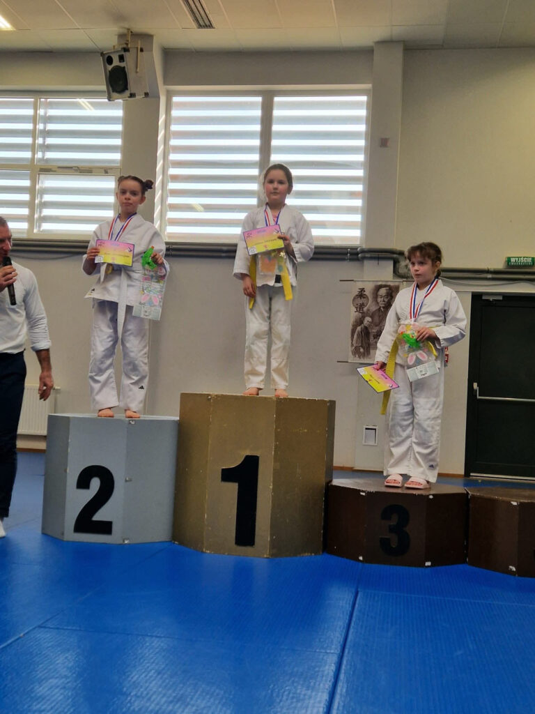 Zawodnik TS Judo Gryf Słupsk stojący na najwyższym stopniu podium z medalem i dyplomem w rękach.